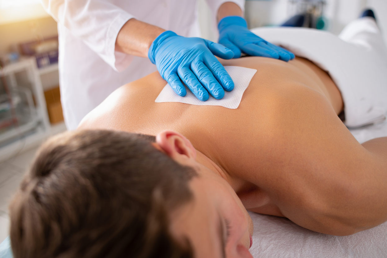 Врач в перчатках накладывает стерильную повязку на спину пациента после процедуры кодирования препаратом Торпедо